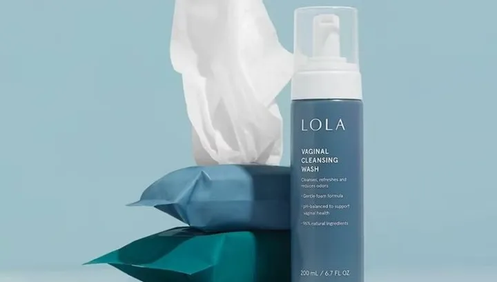 Vaginal cleansing wash bottle next to packets of wipes against a light blue background.